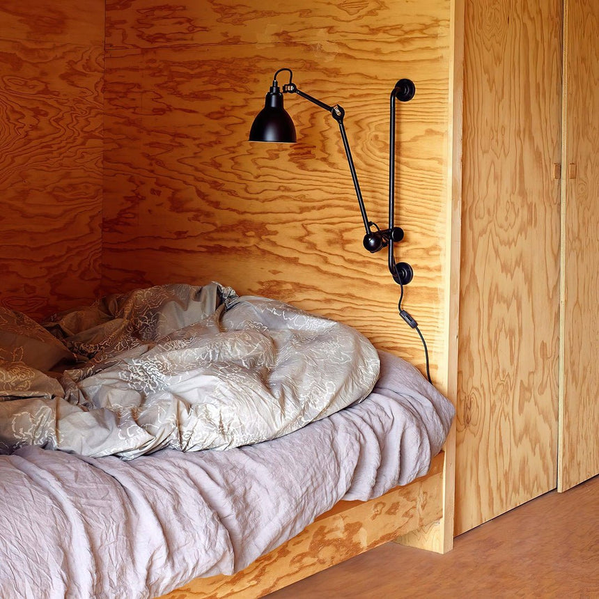 The lamp lit in a plywood bed nook above rumpled bed linens