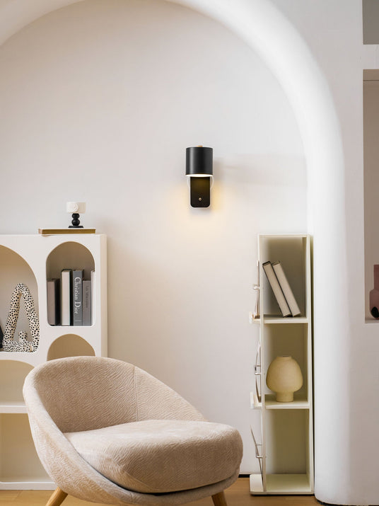 Lit beside an armchair in an alcove of arched shelving holding books and vases