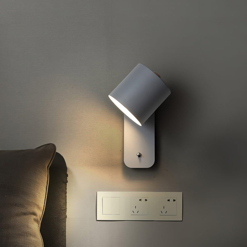 Lit beside a bed against a dark wall, the beam falling across a linen cushion