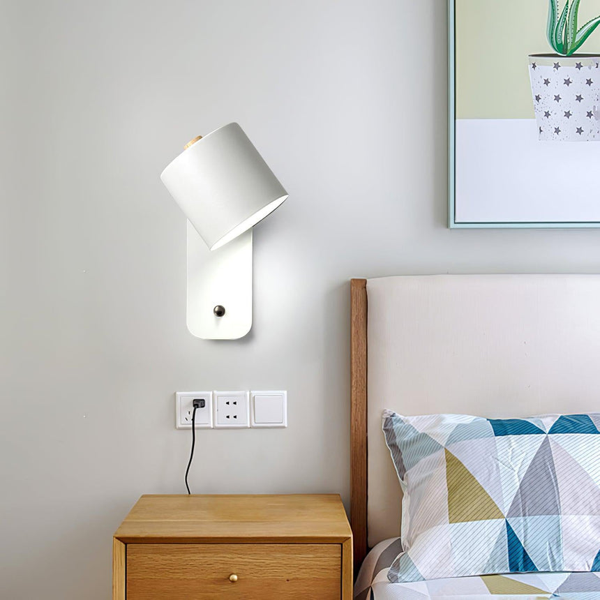 Lit over a wood nightstand beside a bed with patterned cushions and a print