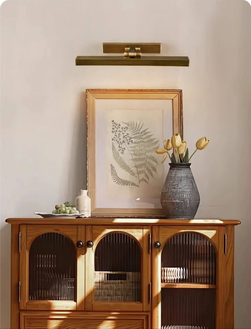 Brass bar lit over a framed print above a cane cabinet with yellow tulips