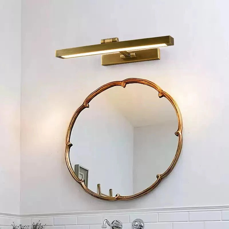 Brass bar lit above a scalloped round mirror in a tiled bathroom