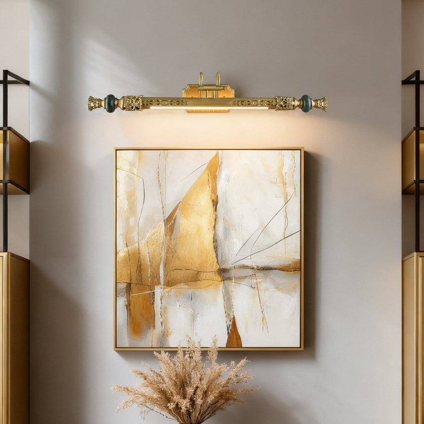 Ornate brass bar lit above a framed abstract canvas on a pale wall