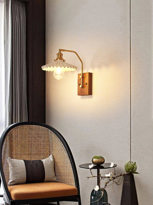 Brass and walnut sconce lit on a wall beside a rattan chair and table