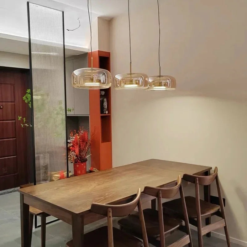 Three amber bell pendants lit above a wooden dining table and chairs