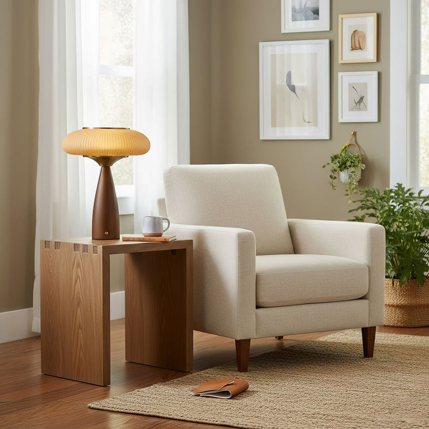 Amber glass table lamp lit on a side table beside a pale armchair