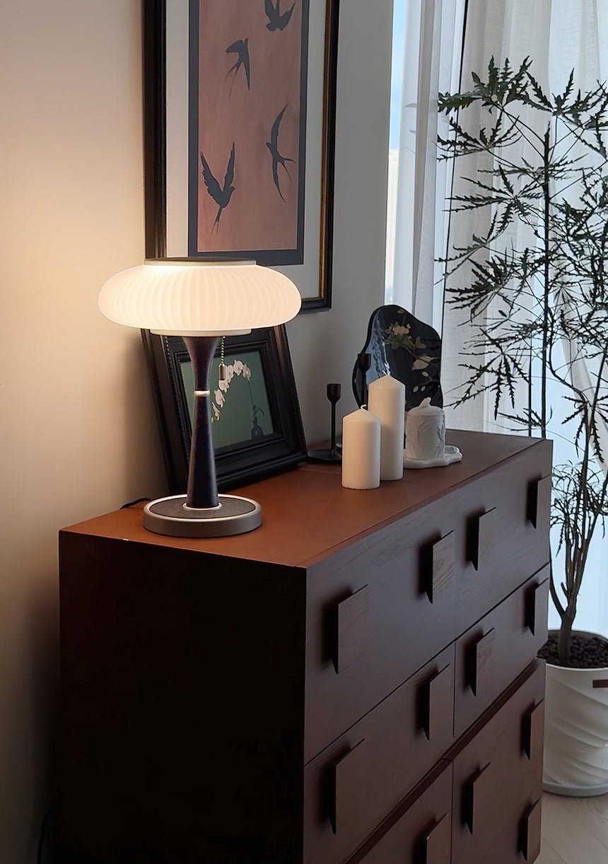 White glass table lamp lit on a red chest beside framed pictures