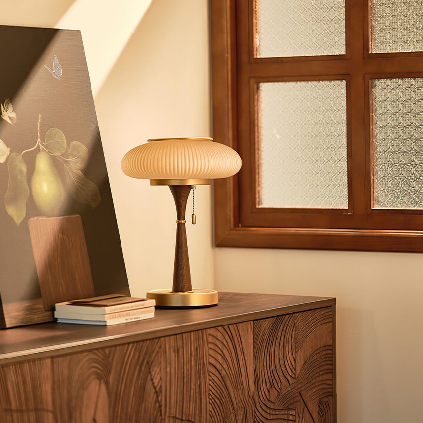 Amber glass table lamp lit on a sideboard beside leaning artwork