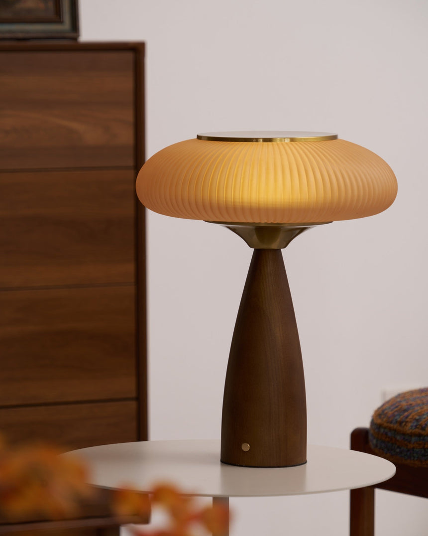 Amber glass table lamp lit on a white side table in a pale room