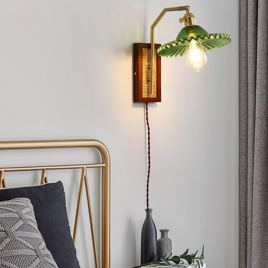 The sconce with a green shade lit above a bed with a metal headboard