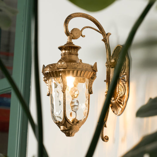 The lantern lit on a pale wall beside a green door frame and foliage
