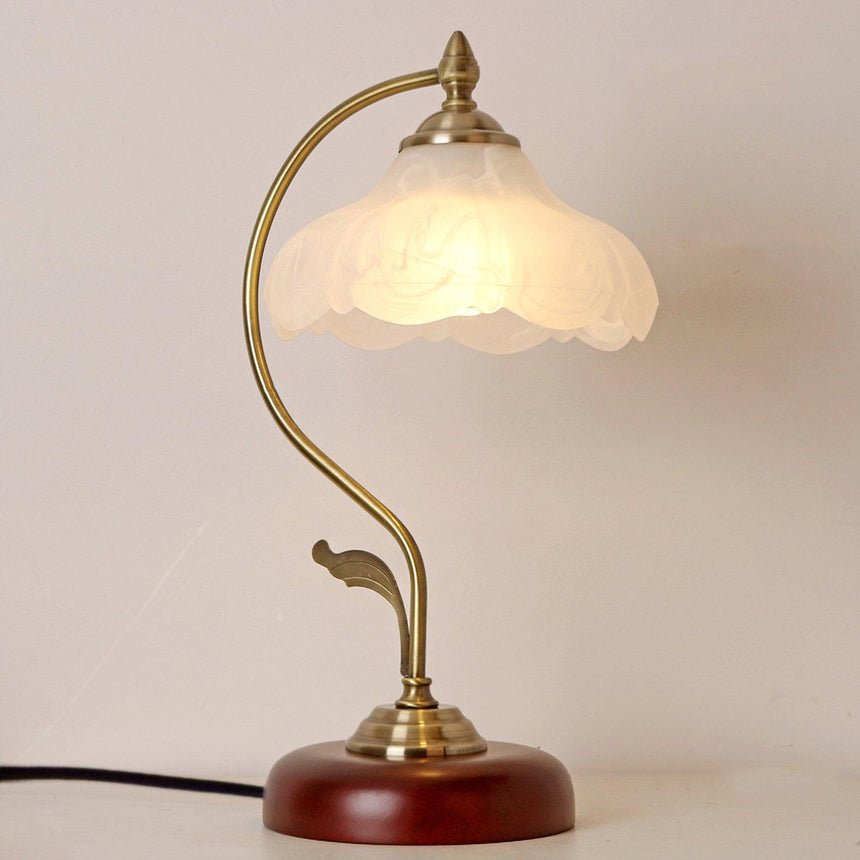 Flower shade lamp lit warm against a pale wall, seen up close