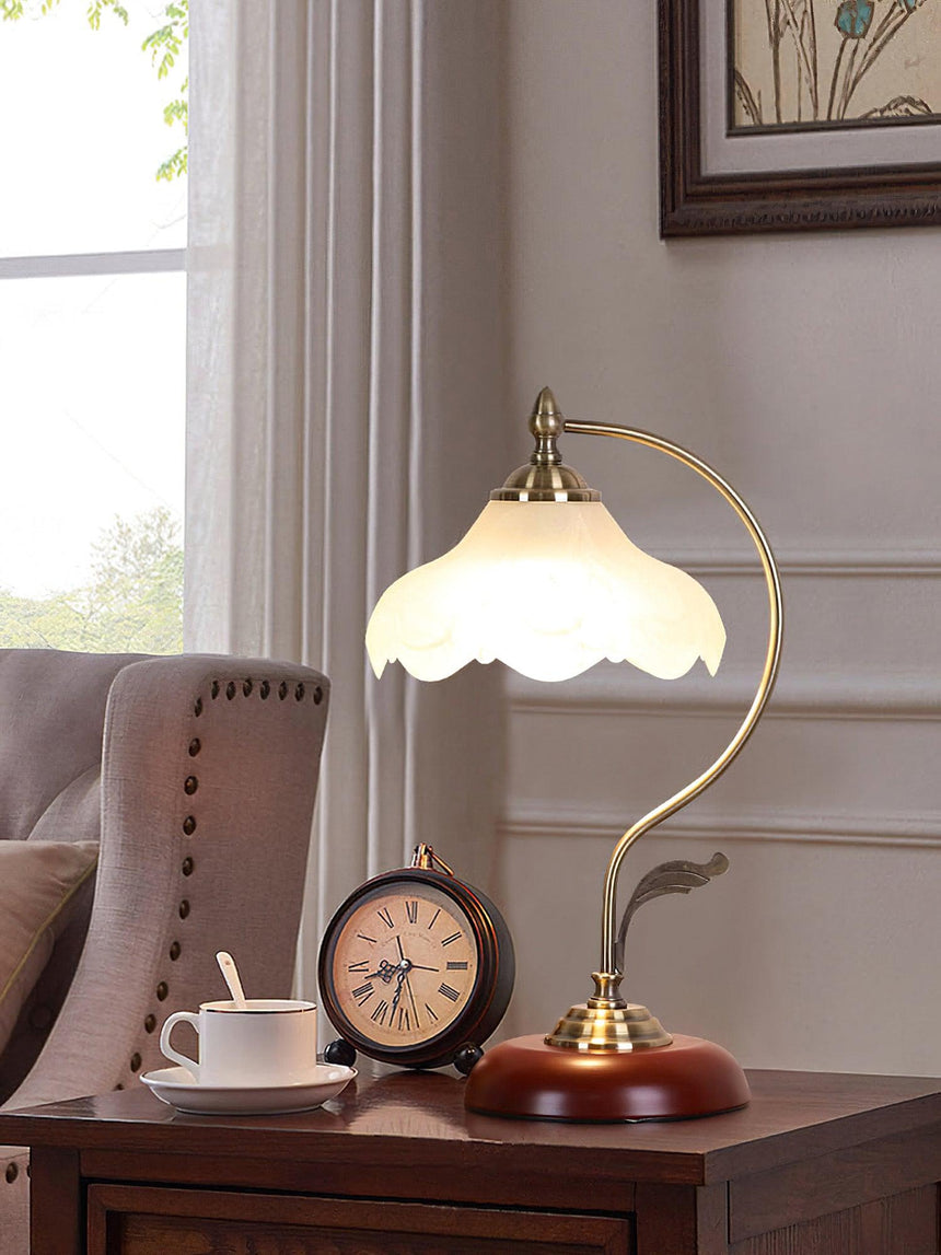 Flower shade lamp lit on a nightstand beside a small round clock