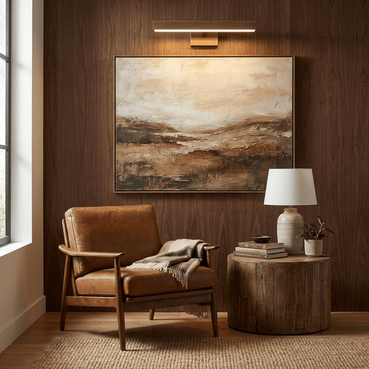 Brass bar lit above a framed landscape on a dark wood wall beside a leather chair