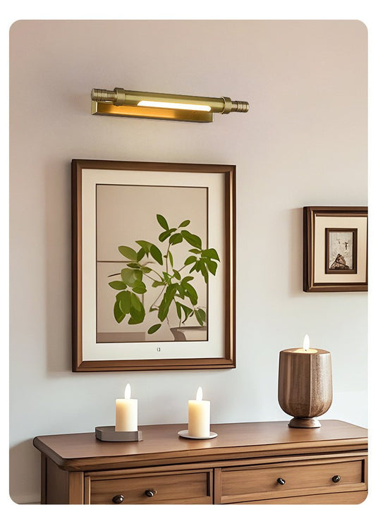 Brass tube lit over framed prints above a wood dresser with candles