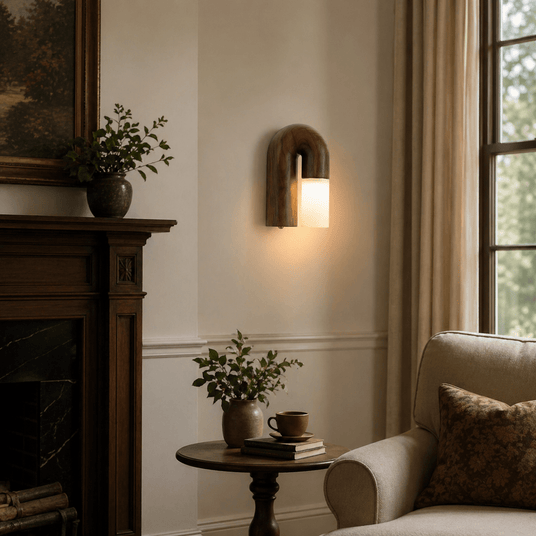 Sconce lit in a living room beside a marble fireplace and a tall window