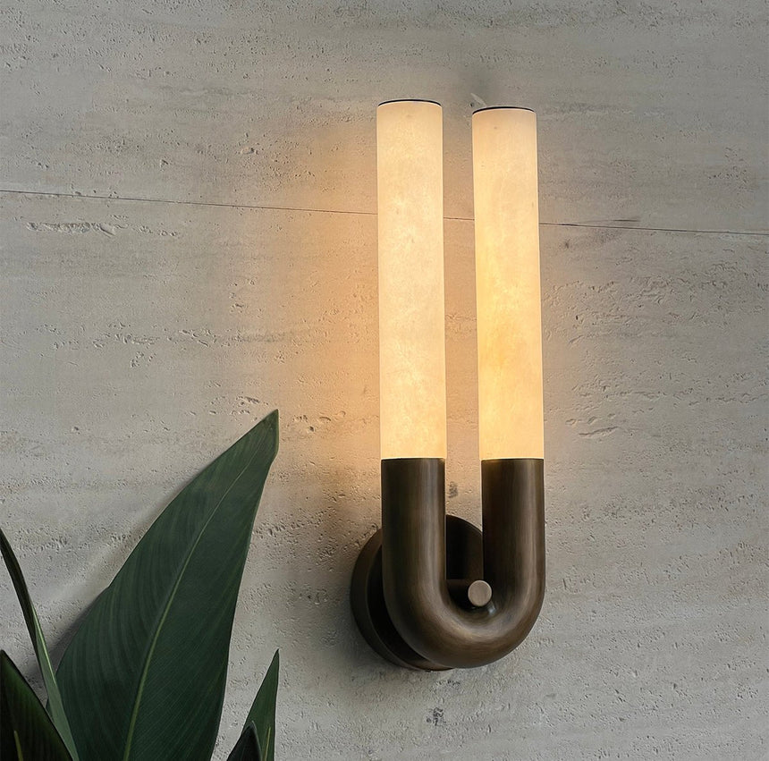 The sconce lit on a green plaster wall beside broad leaves