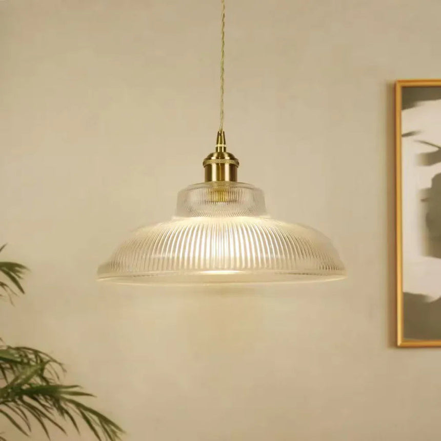 Clear prismatic shade hanging in front of a framed print on a pale wall