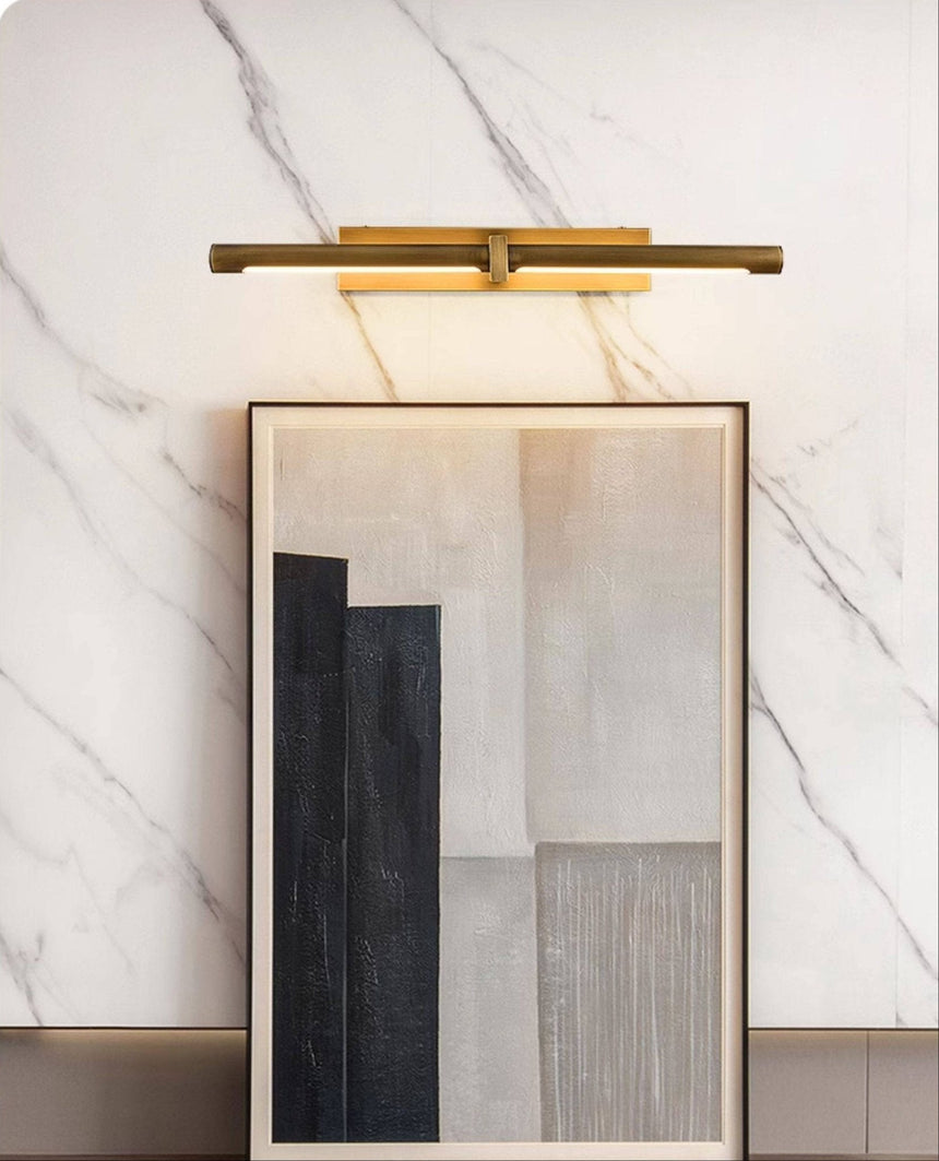 Brass twin bar lit over framed artworks leaning against a marble wall
