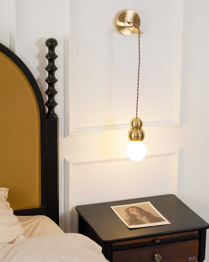 The gold ball light hanging beside a bed above a nightstand with a print
