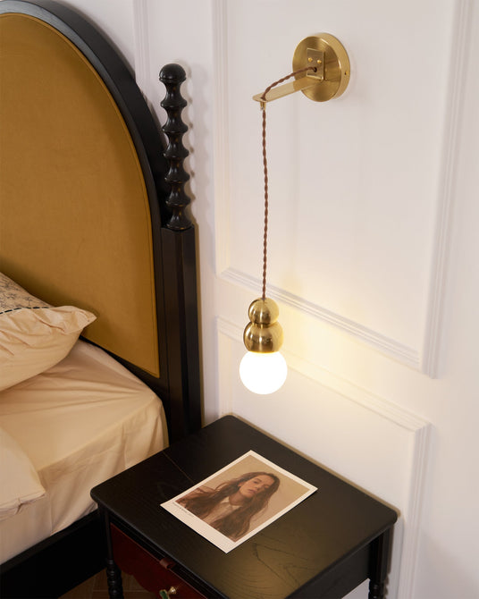 The gold ball light lit above a black nightstand beside an arched headboard