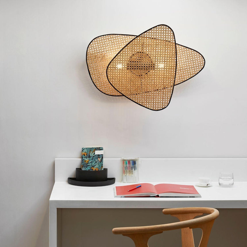 The cane sconce lit above a white desk with an open book and a wood chair