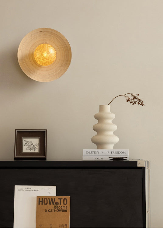 Sconce lit above a black dresser with a framed print, books and a vase