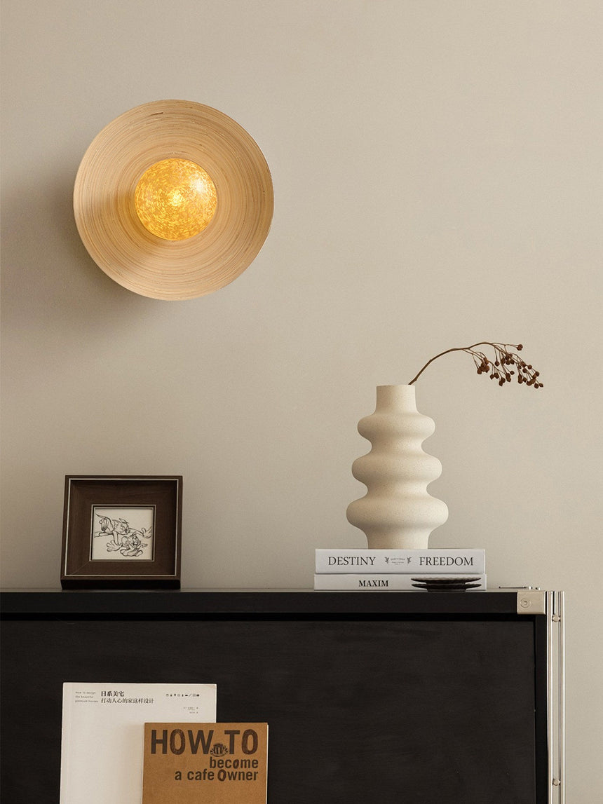 Sconce lit above a dresser holding a ribbed vase, a framed print and books