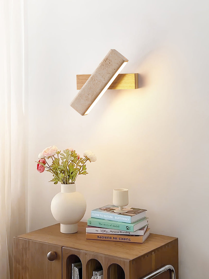 Sconce lit beside a wood nightstand holding flowers, a candle and books