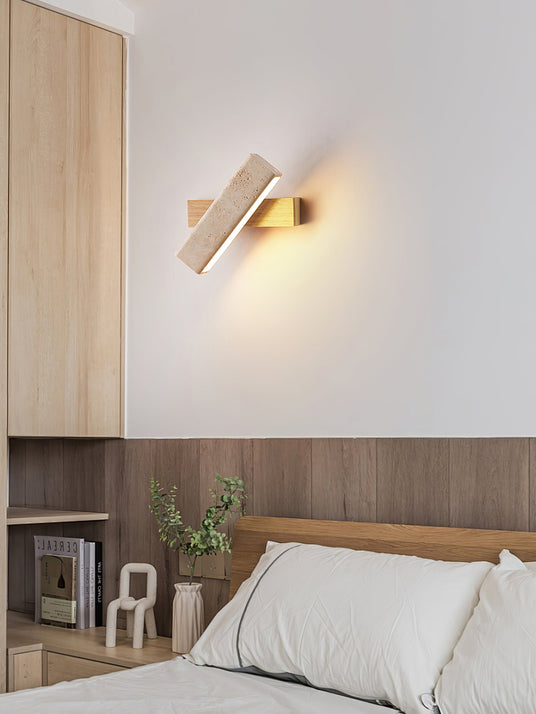 Sconce lit above a bed against a wood panel wall with books on a shelf