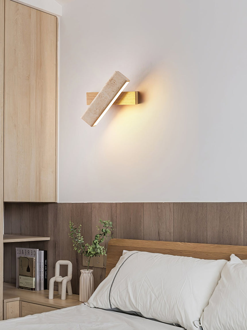 Sconce lit above a bed against a wood panel wall with books on a shelf