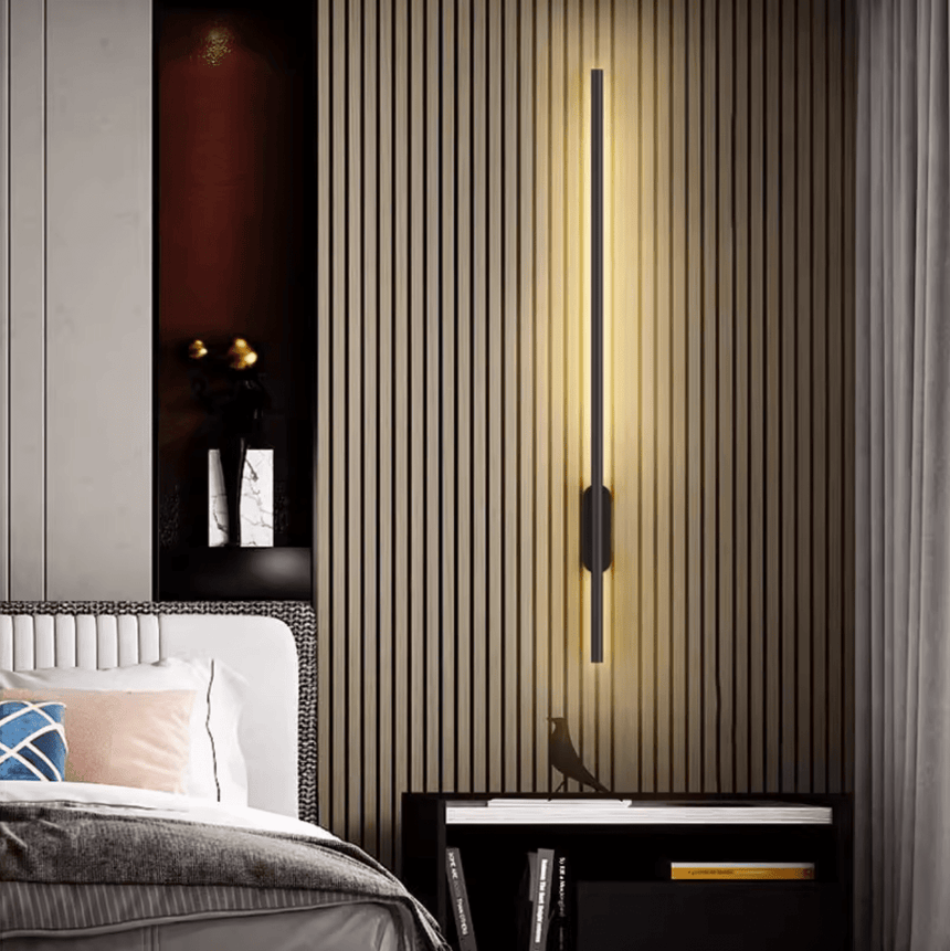 Lit vertically on a fluted timber wall beside a bed with folded linen
