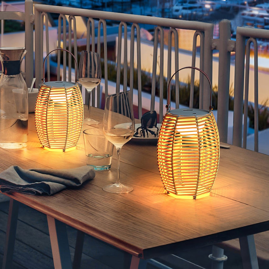 Two lit on a timber table beside glasses on a balcony at dusk