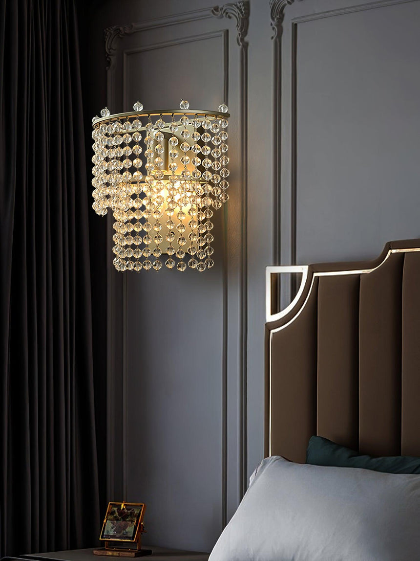 The beaded sconce lit on a dark paneled wall beside a channel tufted headboard