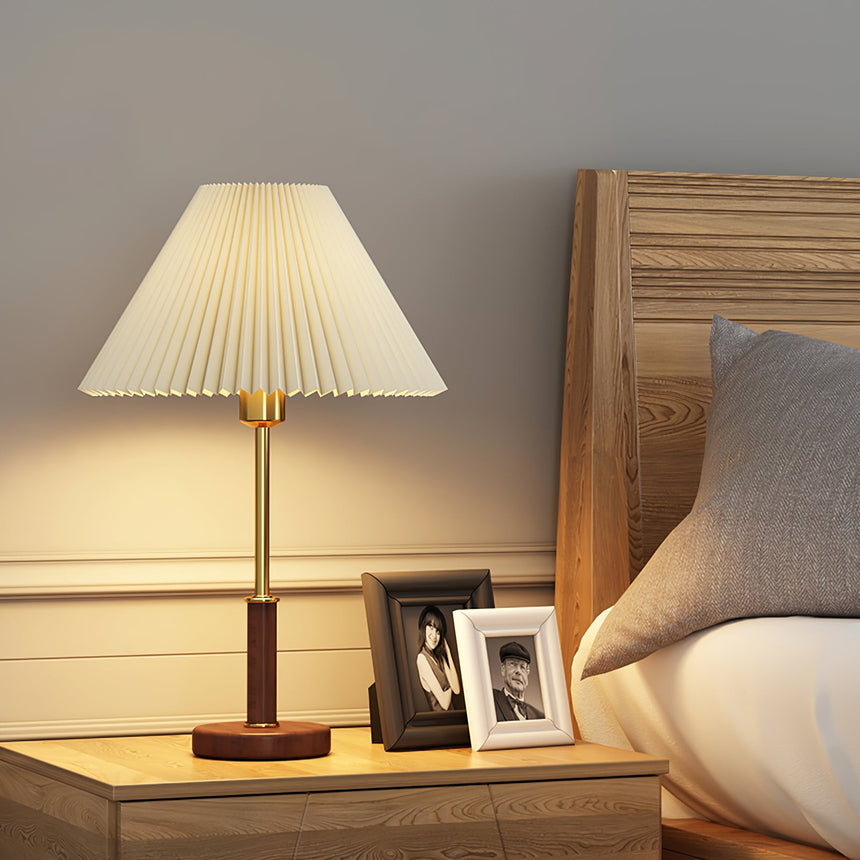 Pleated shade bedside lamp lit beside a bed and two framed photos