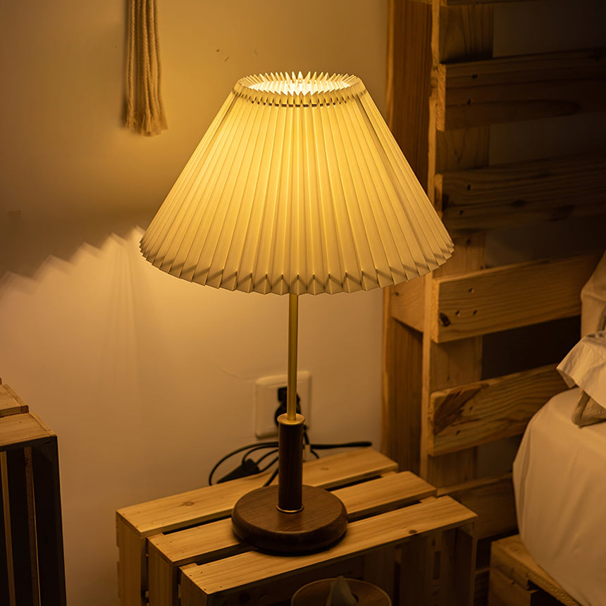 Pleated shade bedside lamp lit on a wooden crate beside a bed