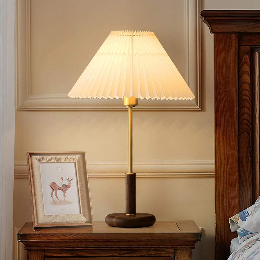Pleated shade bedside lamp lit in a warm bedroom beside a framed print