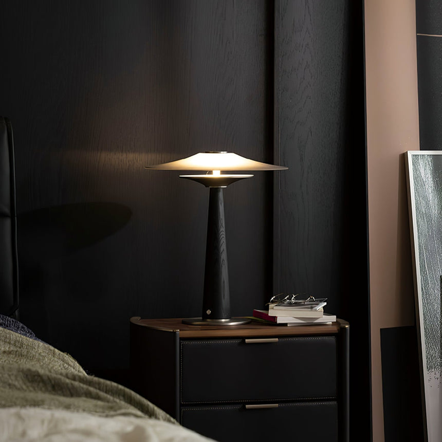 Bedroom table lamp lit on a nightstand beside rumpled bedding
