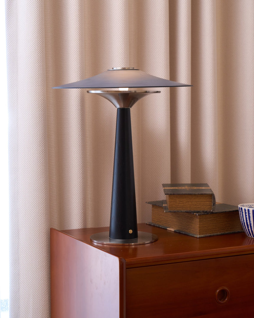 Bedroom table lamp lit on a chest in front of a pale curtain