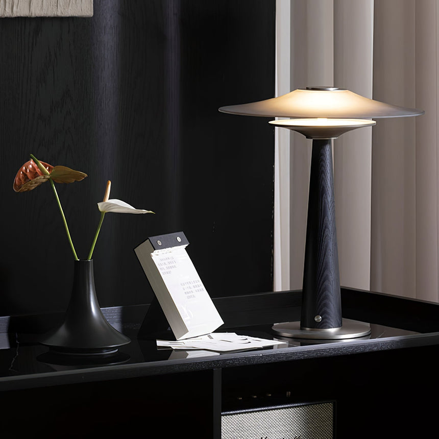 Bedroom table lamp lit on a desk beside a tablet and a notebook