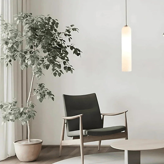 A white tube pendant lit beside an armchair and a large plant