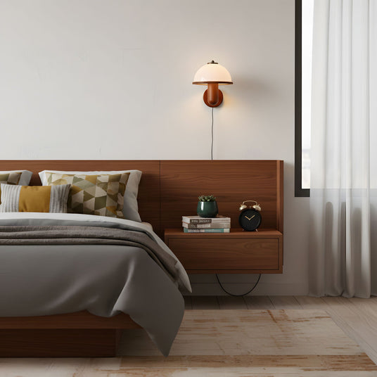 Oak wall lamp lit above a floating nightstand beside a made bed