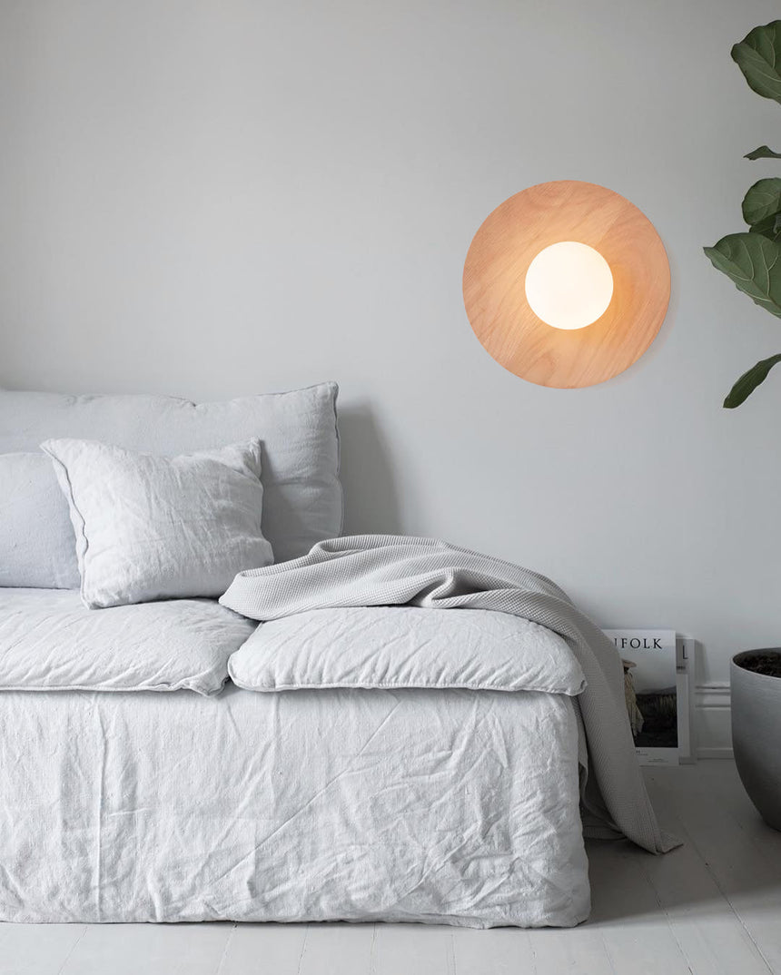 Lamp lit on a bedroom wall above a bed with a plant in the far corner