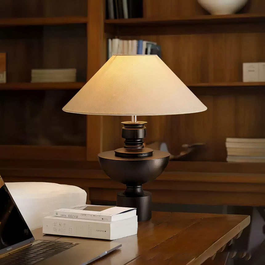 Beige table lamp lit on a desk beside a laptop and a stack of books