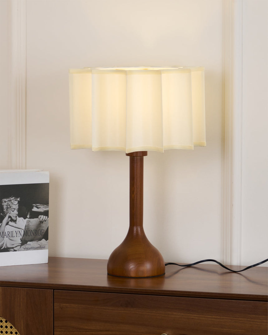 Beige table lamp lit and seen at an angle on a walnut sideboard