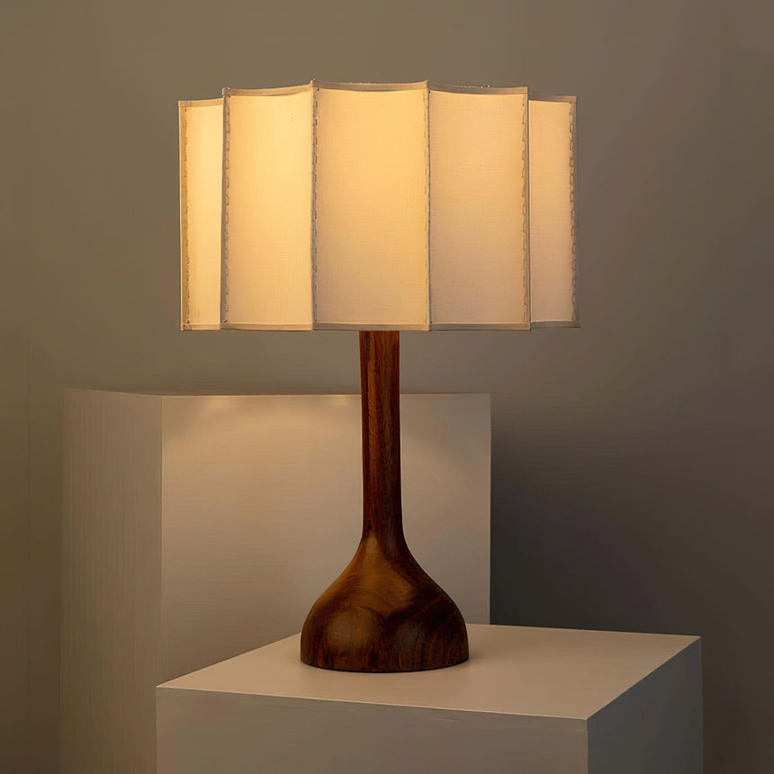 Beige table lamp lit on a white plinth against a warm wall