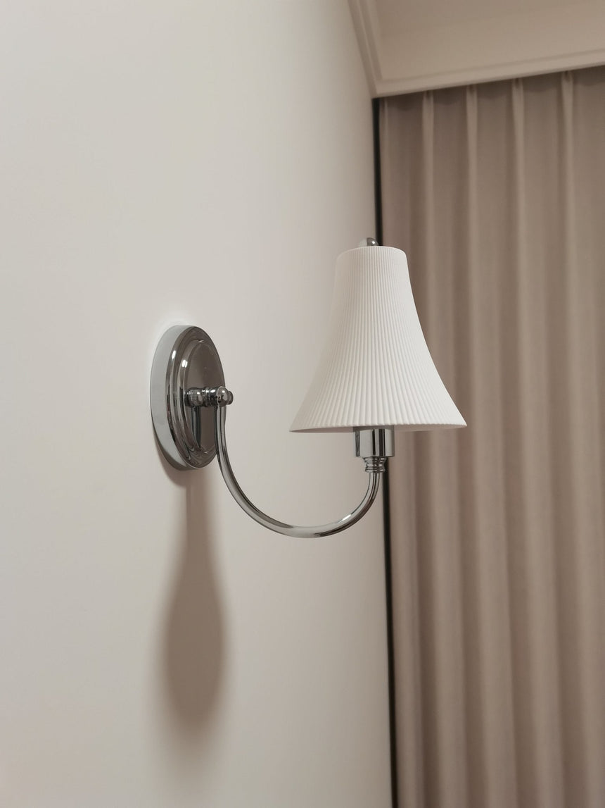 The sconce unlit beside a brown curtain, the chrome arm curving up