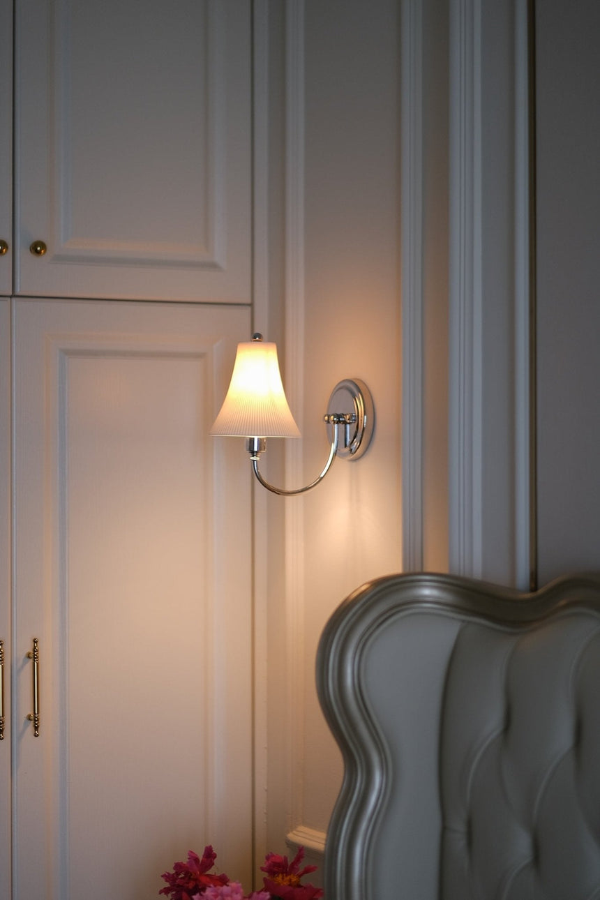 The sconce lit beside a tufted headboard, white wardrobe doors and pink flowers