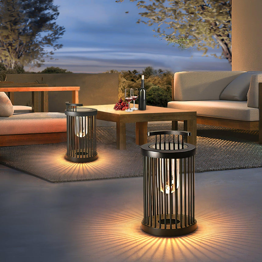 Two lanterns lit on a paved terrace beside a timber table and a sofa