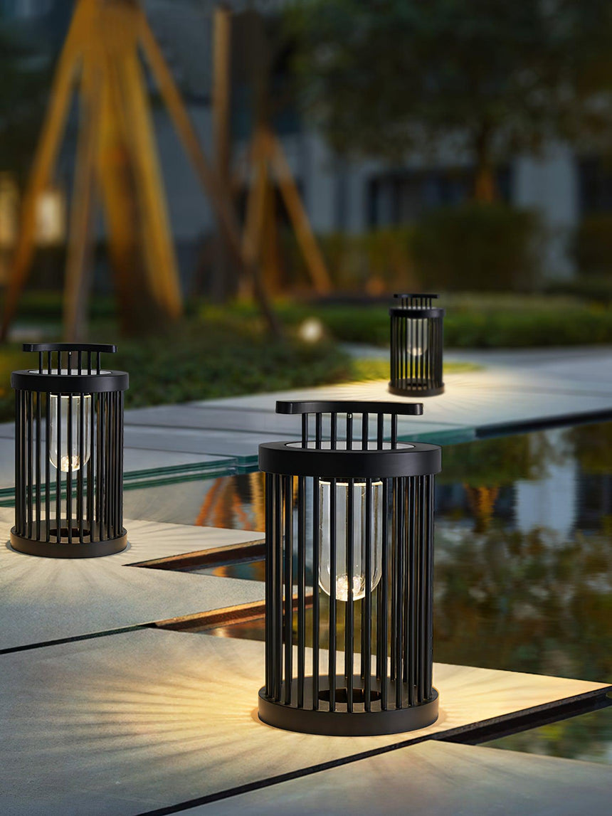 Two lanterns lit on a paved garden walkway with planting behind them
